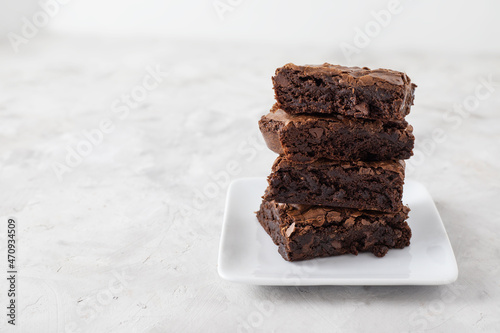 Stack of chocolate brownies on white plate on concrete table with copy space