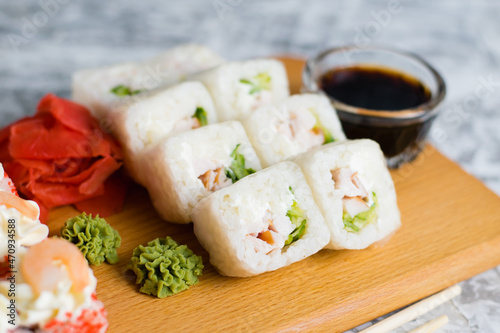Delicious sushi rolls with chicken, cheese, shrimp, red ginger, wasabi and soy sauce on a wooden board on a light background with copy space
