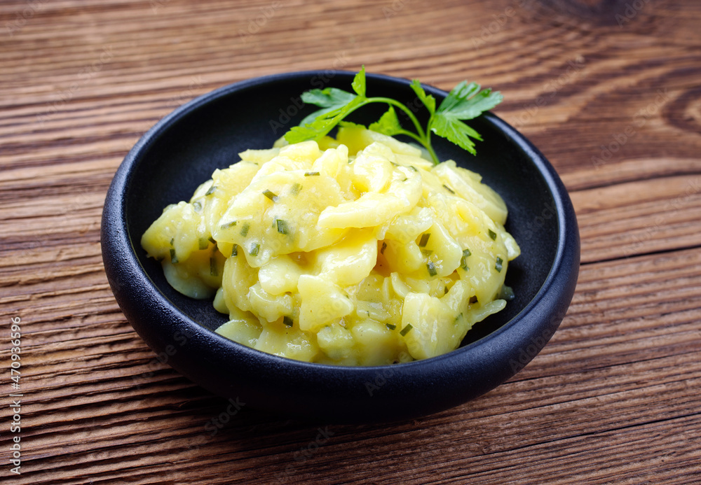 Traditional German potato salad with onion and chives served as a close-up in a design bowl on a rustic wooden board Traditional German potato salad with onion and chives served as a close-up in a design bowl on a rustic wooden board