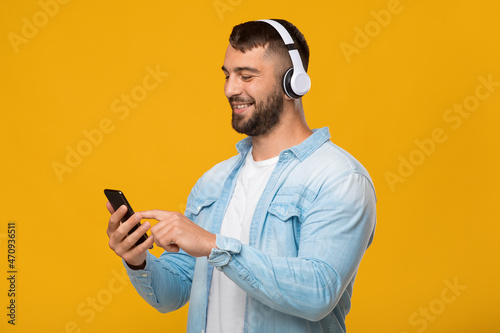 Happy adult european guy in headphones enjoying favorite music, typing on smartphone © Prostock-studio