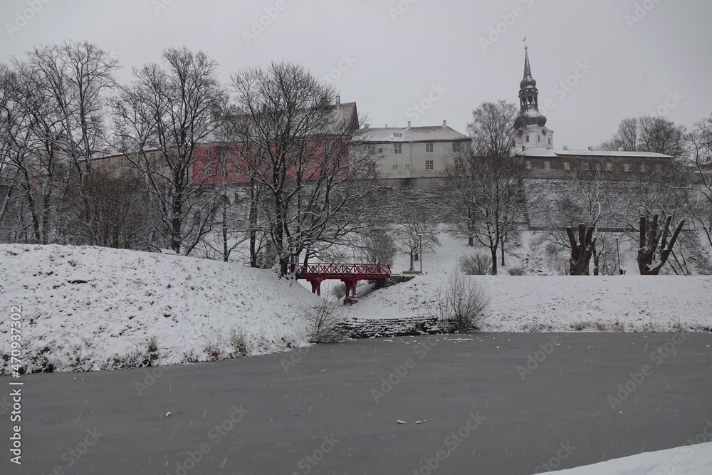 Naklejka premium Winter view to Tallinn medieval old town on Toompea hill. Snelli Toompark with red bridge over water canal. A lot of snow. Trees with no leaves. Tallinn, Estonia. January 2021