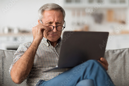 Older Male Squinting Eyes Using Laptop Wearing Eyeglasses At Home photo