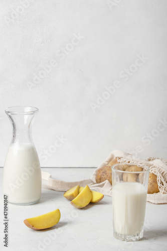 In a bottle and in a glass, the drink is vegetable, vegetable potato is not milk. Nearby there are potatoes cut into wedges, on a white background, and a knitted string bag with whole potatoes