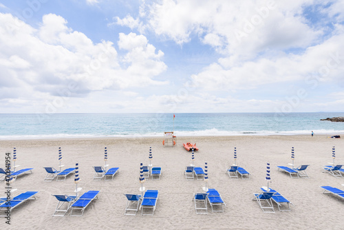 Finale Ligure. May 21, 2021. View from the Lungomare Italia street on an empty stretch of beach with blue sunbeds and umbrellas and a lifeguard spot with a small rescue boat.