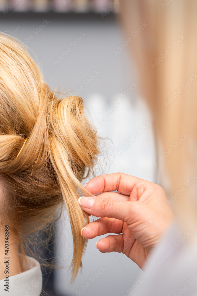 Fototapeta premium Close-up hairdresser styling blonde hair on the back of the head in a beauty salon