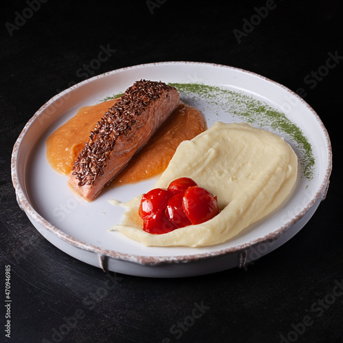 Fish with potato garnish on a plate on a dark background