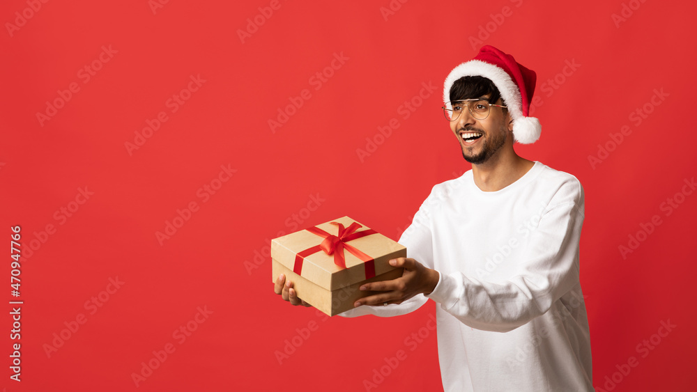 Positive middle eastern man in santa hat giving gift box Positive middle eastern man in santa hat giving gift box