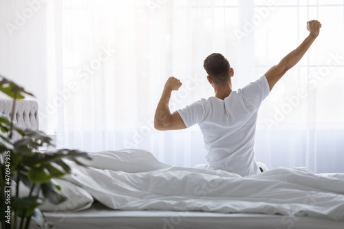 Fotografia Man Stretching In Bed After Waking Up In The Morning, Rear View