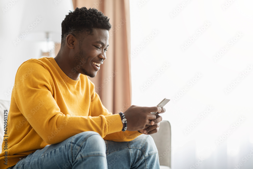 Happy black guy chatting with girlfriend, using smartphone at home