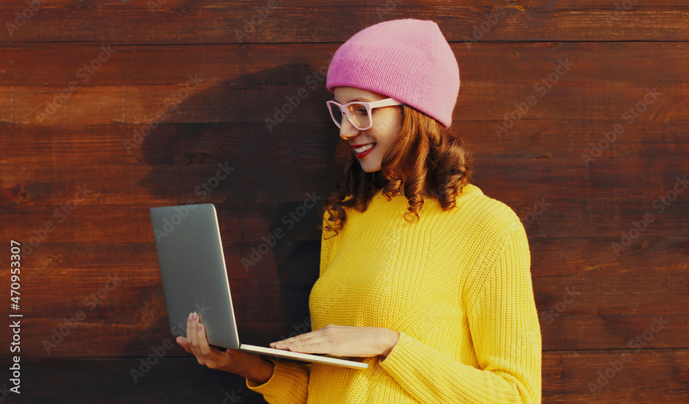 Portrait of stylish modern young woman working with laptop wearing a colorful clothes on wooden wall background Portrait of stylish modern young woman working with laptop wearing a colorful clothes on wooden wall background