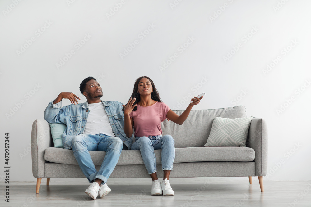 Sweaty young black woman switching on air conditioning at home Sweaty young black woman switching on air conditioning at home