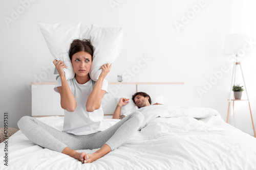 Tableau sur toile Sad caucasian millennial wife freaking out, sitting in bed, covering ears with p