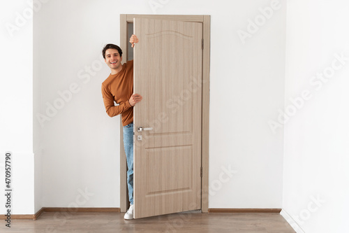Cheerful guy looking out of door standing in doorway