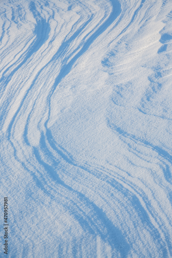 Fototapeta premium Beautiful winter background with snowy ground. Natural snow texture. Wind sculpted patterns on snow surface.