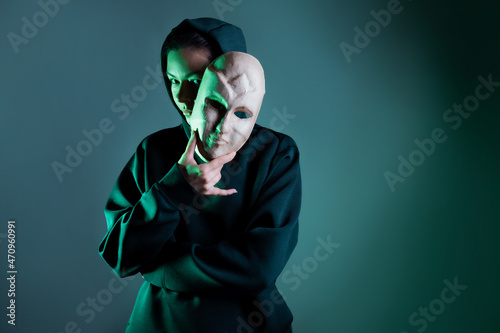 Hiding behind a mask, a young woman in a dark hoodie hides her face with a mask, privacy on the Internet, the concept of information security