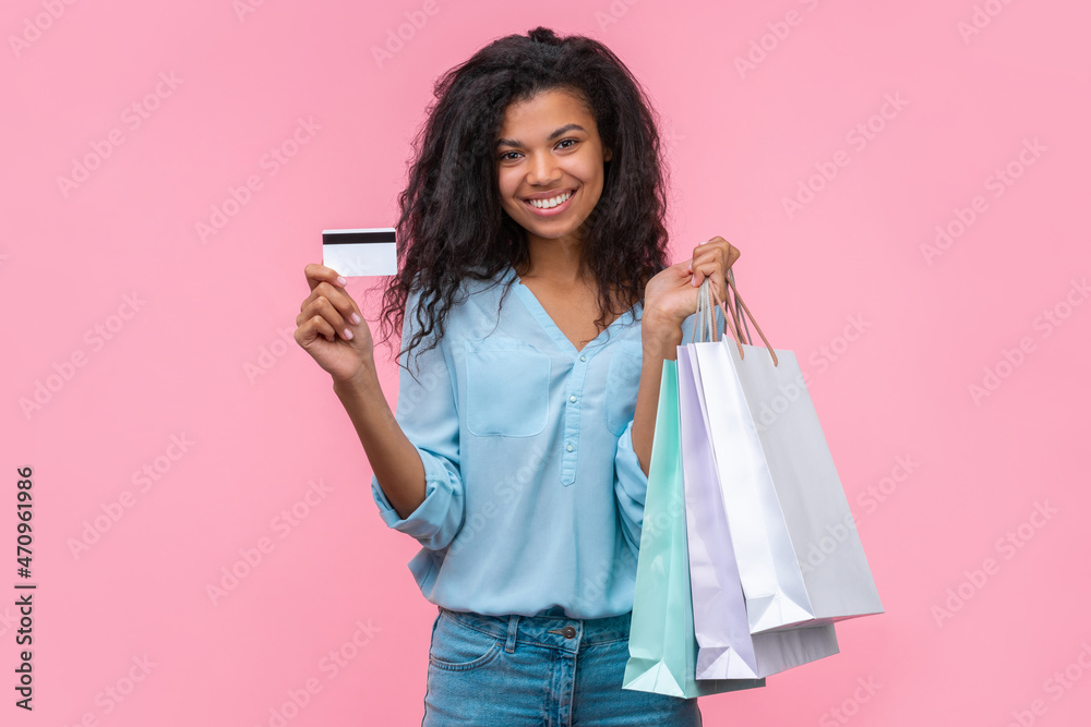 Half-length portrait of attractive stylish smiling elegant dark skinned woman posing with with shopping bags and credit card in hands while isolated over pink background Half-length portrait of attractive stylish smiling elegant dark skinned woman posing with with shopping bags and credit card in hands while isolated over pink background