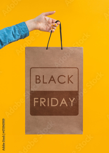 Vertical cropped shot of female hand holding craft paper bag on vivid orange yellow background