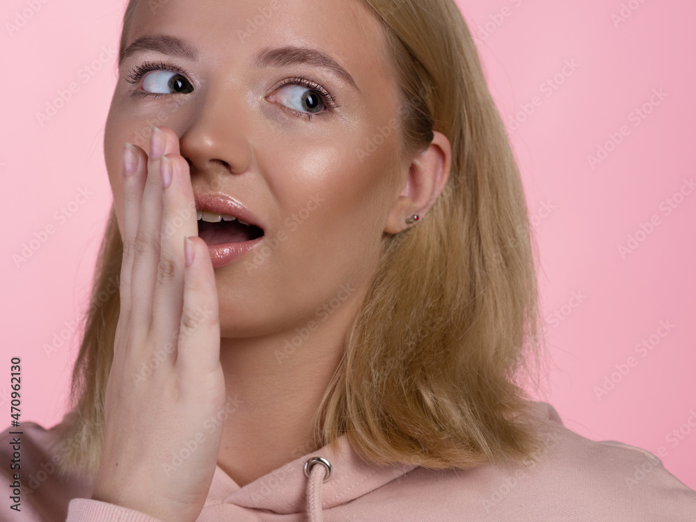cute young blonde in a pink hoodie is shocked and surprised, says wow. The emotion of surprise, hands touching the face. portrait on a pink background, close-up cute young blonde in a pink hoodie is shocked and surprised, says wow. The emotion of surprise, hands touching the face. portrait on a pink background, close-up