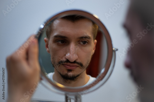 Foto A guy with a patchy beard looks in the mirror