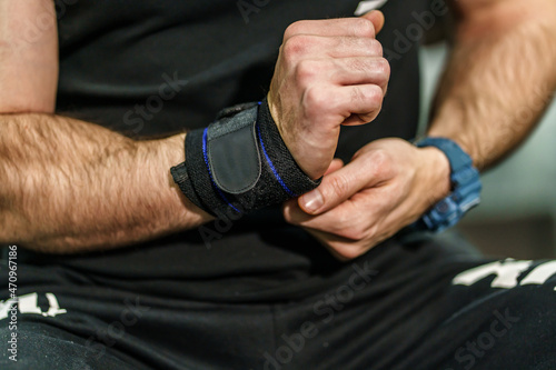 Close up on hands of unknown man holding and putting on and adjusting wrap bandages on wrists for powerlifting body building training sport equipment at the gym