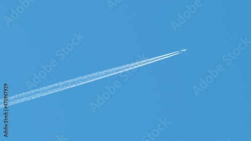 Distant passenger jet plane flying on high altitude on clear blue sky leaving white smoke trace of contrail behind. Air transportation concept
