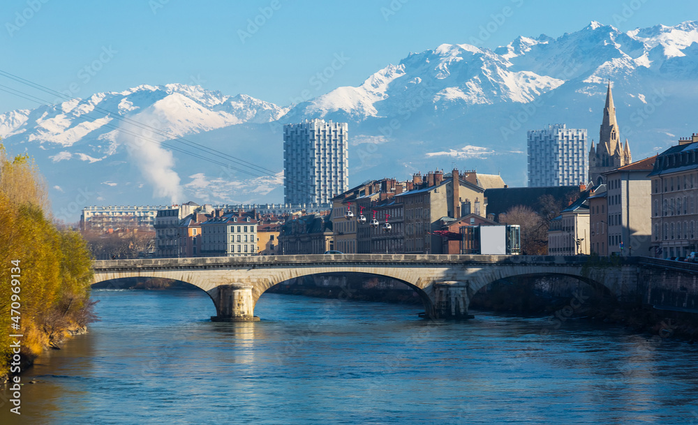 Naklejka premium Cityscape of Grenoble with famous cable car against backdrop of snowy Alps in sunny day, France