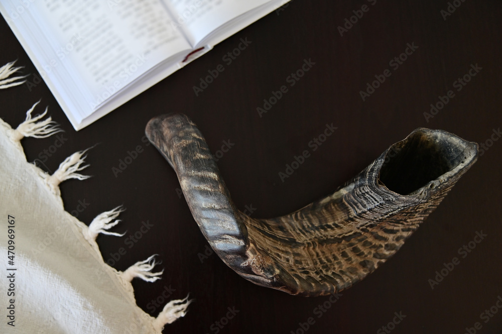 Flat lay of Shofar (rams horn) Tallit and Jewish prayer book on a wooden table.