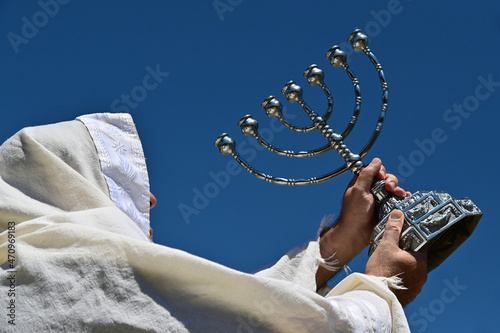 Orthodox Jewish man holding a temple Menorah against clear blue sky. photo