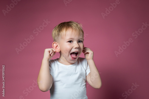 Caucasian boy makes faces  shows tongue  looking at camera on pink background