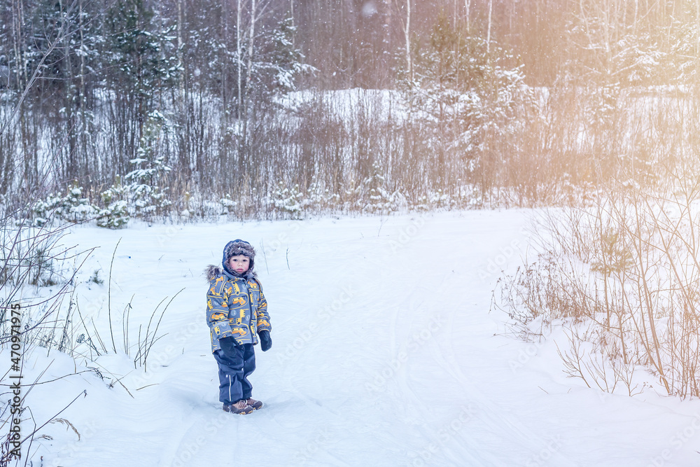 A boy in warm clothes stands in the middle of a winter forest