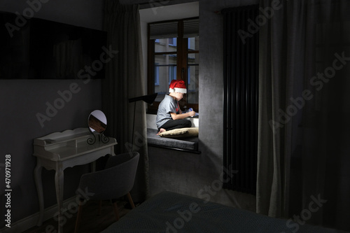 Boy wearing a santa claus hat writes a letter asking for a gift for christmas in a dark room. photo