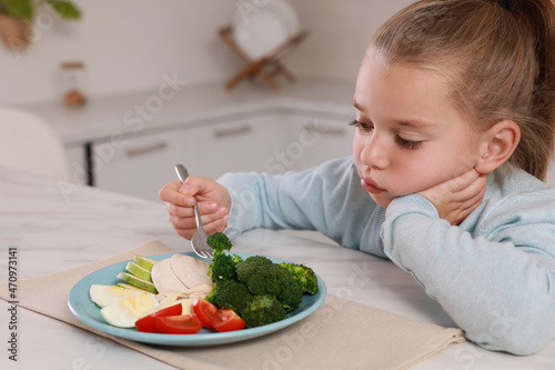 Cute little girl refusing to eat dinner in kitchen