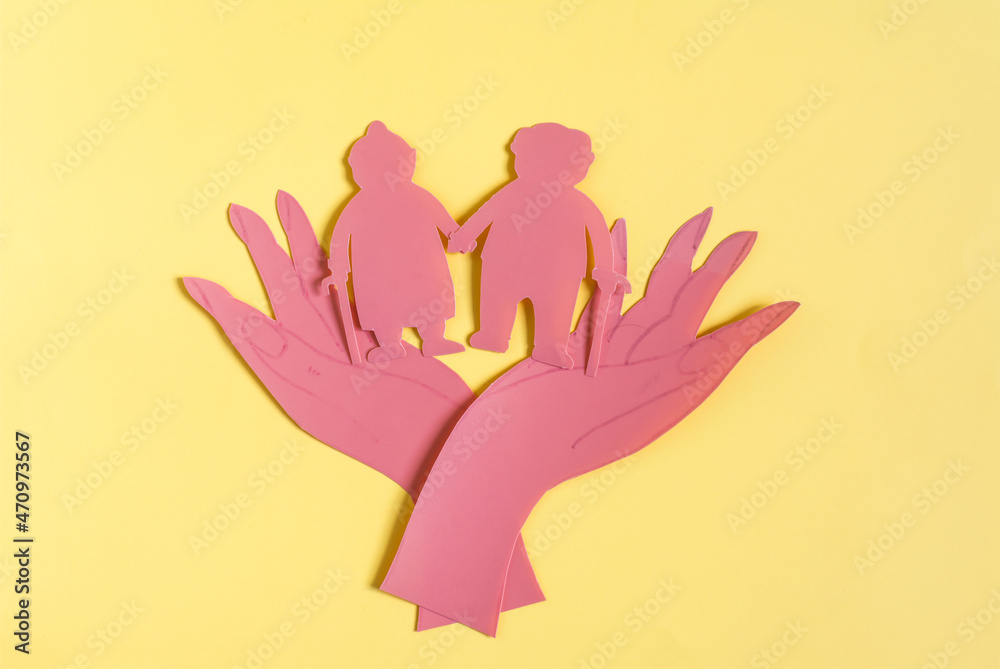 Obraz premium Cardboard figurines open palms of hands hold two elderly people. The concept of protecting the elderly and pensioners