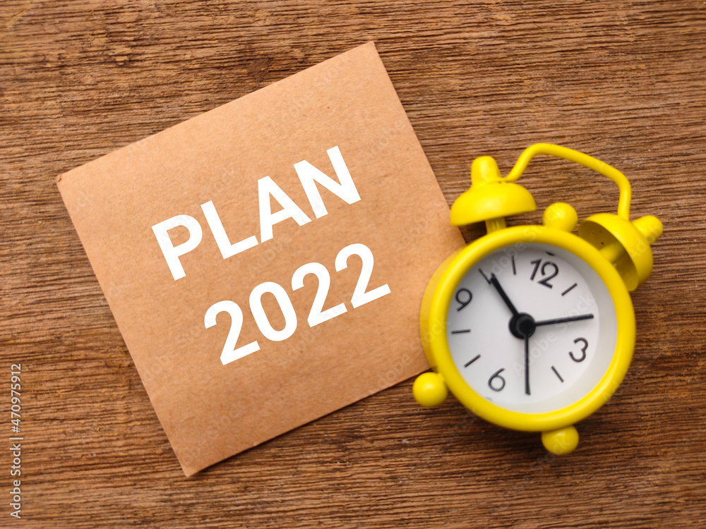 Alarm clock and brown card with text PLAN 2022 on wooden background. Alarm clock and brown card with text PLAN 2022 on wooden background.