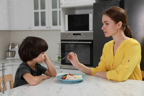 Mother feeding her son in kitchen. Little boy refusing to eat dinner photo