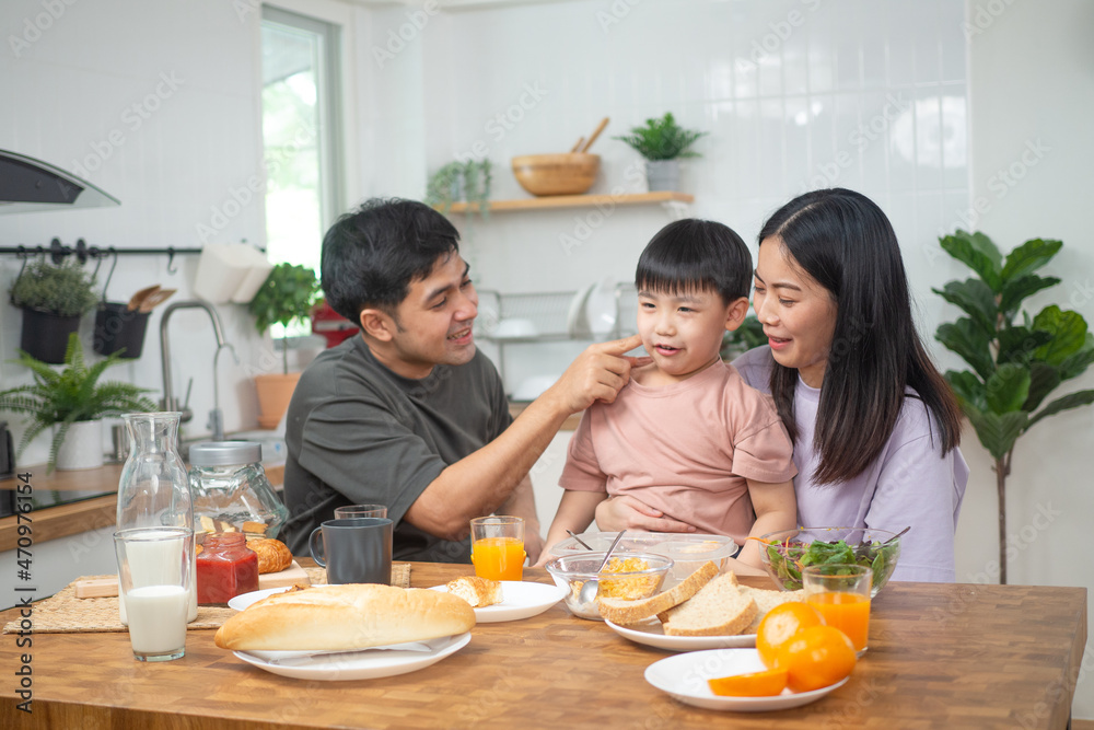 Asian family breakfast at home. Parents and children enjoy eating together, talking with laughter and good atmosphere. Father plays with son playfully at kitchen table. Asian family breakfast at home. Parents and children enjoy eating together, talking with laughter and good atmosphere. Father plays with son playfully at kitchen table.