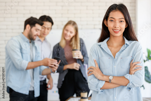 Positive Asian female manager standing near group of multiracial coworkers discussing project while working together in light conference room