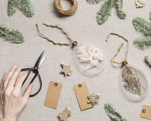 Diy baubles filled dried florals, grass. Glass Christmas ornaments on rustic cloth texture background. Woman hands hold New Year holiday gift or decoration interior idea