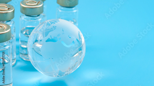 Global vaccines supply, international medical emergency and worldwide vaccination effort concept with glass globe and vaccine doses isolated on blue background with copy space