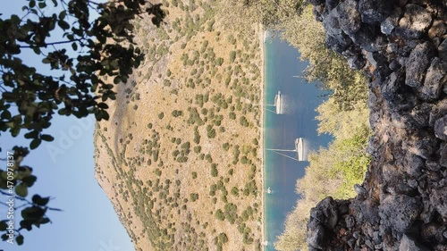 The vertical footage of the picturesque bay near Gemiler island, lonely sail boat in sea, islands near Marmaris, sailing regatta, mountains on background, top view in clear weather photo