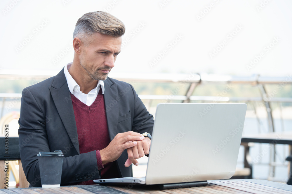 Serious professional man check time on watch working on laptop computer outside, punctuality Serious professional man check time on watch working on laptop computer outside, punctuality
