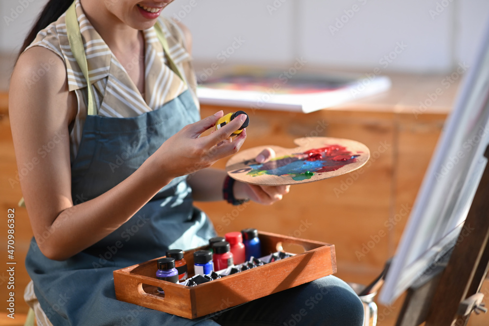 Smiling asian woman holding palette while working on painting in her studio.