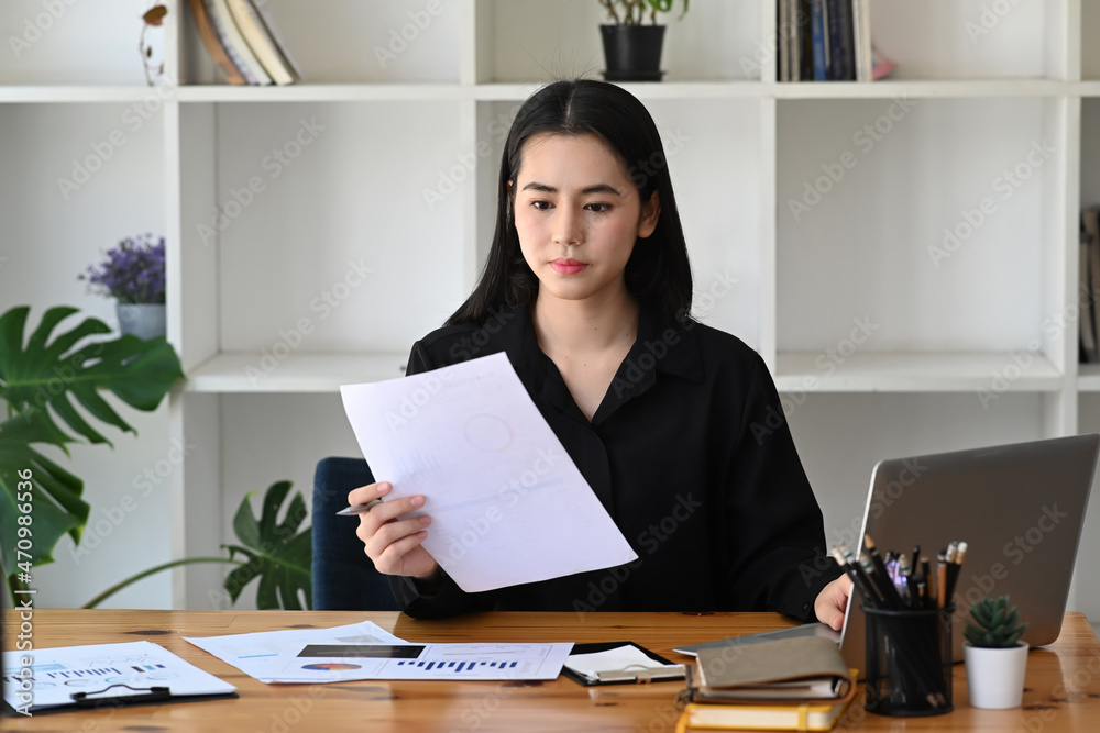 Beautiful businesswoman working with laptop computer and reading reports at office.