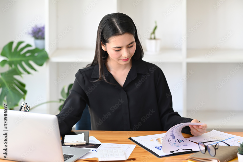 Attractive businesswoman reading documents and working with laptop computer. Attractive businesswoman reading documents and working with laptop computer.