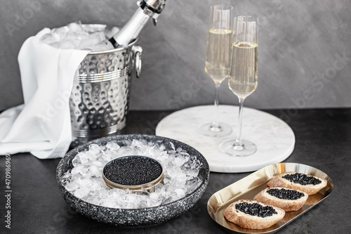 Black caviar in can on ice, caviar sandwich on golden plate, champagne in glass photo