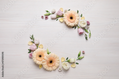 Wreath made of beautiful flowers and green leaves on white wooden background, flat lay. Space for text