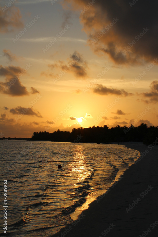 A very beautiful sunset in the Maldives. White sand, calm ocean, orange sky with clouds.
