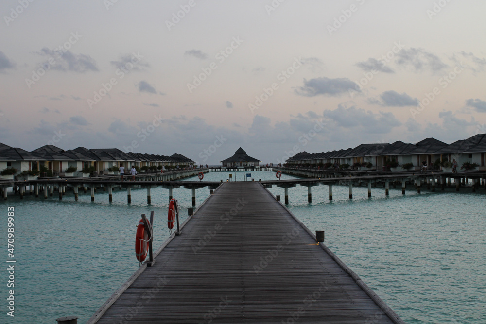 Wooden pier with lifebuoys leading to villas on stilts above the water in the Maldives.