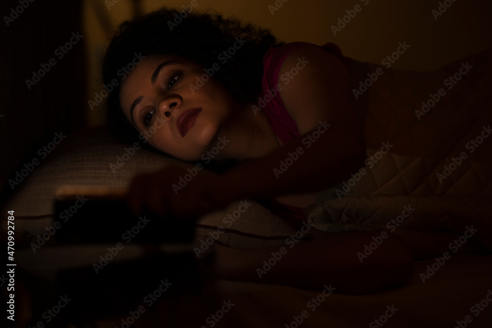 Woman watching smartphone alone at night while lying on bed Woman watching smartphone alone at night while lying on bed