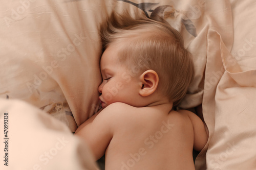 The baby sleeps sweetly in bed lying on his stomach